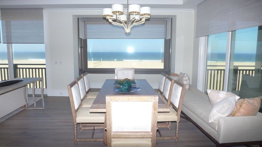 A home on the beach with shades partially drawn over floor-to-ceiling windows.