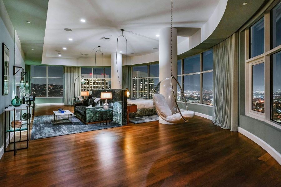 A living area with hanging chairs and picture windows looking over Los Angeles. Draperies hang between the windows.