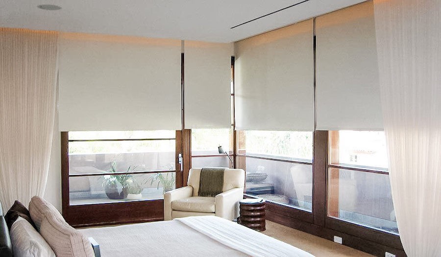 Small bedroom with two windows featuring natural shades bordering a bed. 