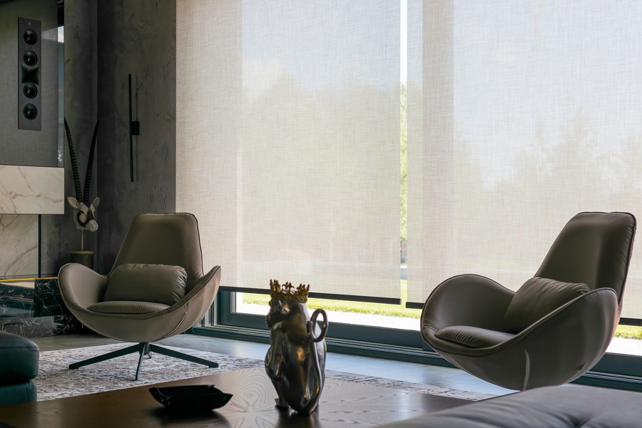  A living room with contemporary chairs with the sunscreen shades drawn.