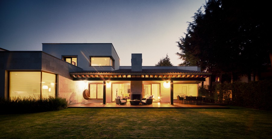 An outdoor pergola illuminated at dusk next to a home.