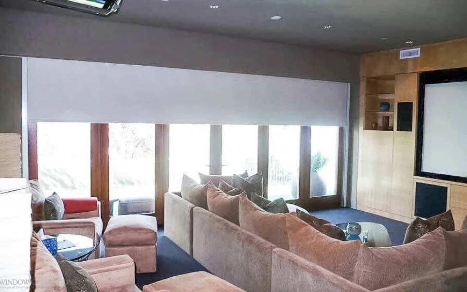 A home theater room featuring couches, a large TV, and motorized shades. 