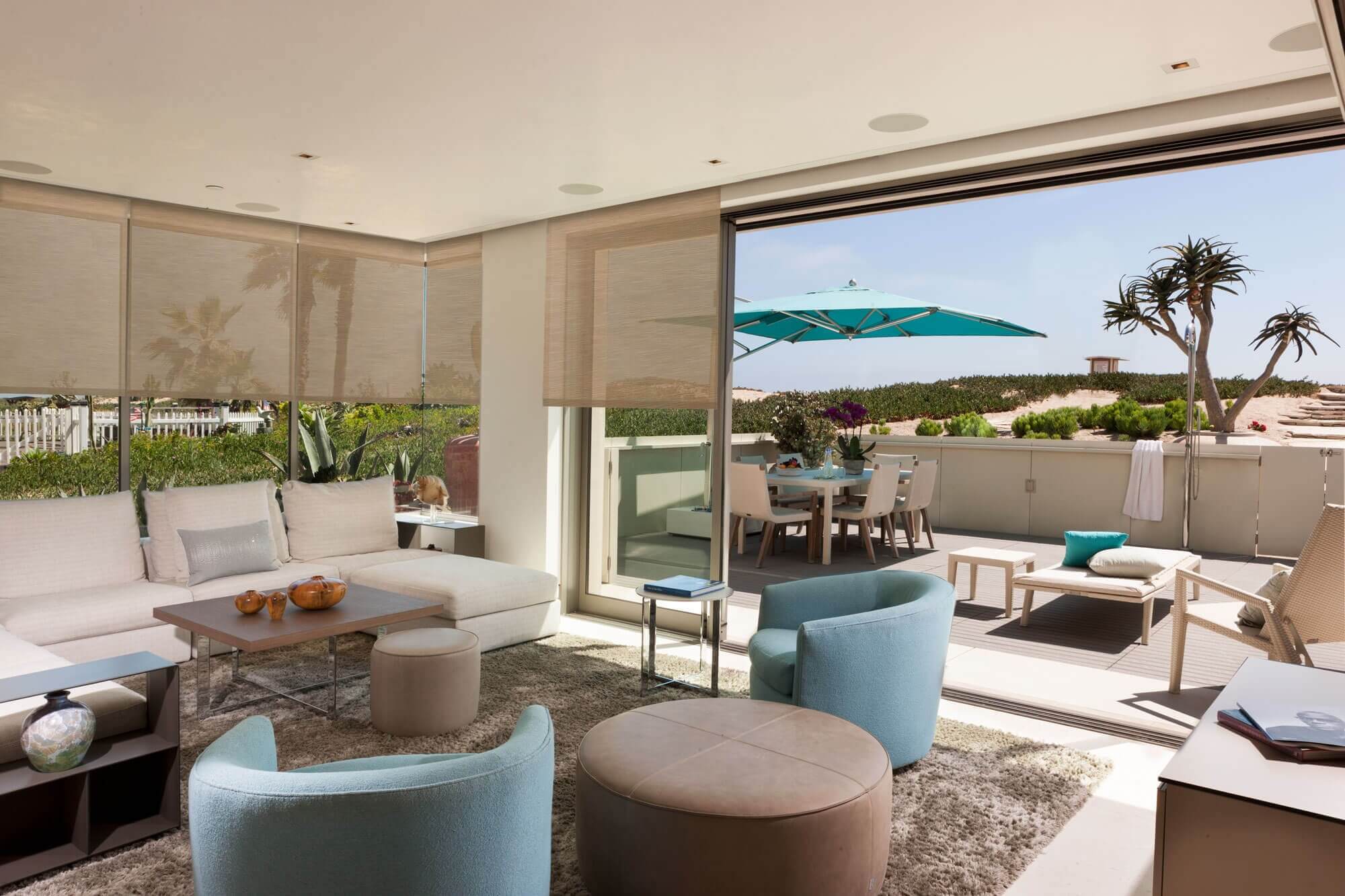 Bright living room with beige sofa, blue chairs, and outdoor patio with turquoise umbrella