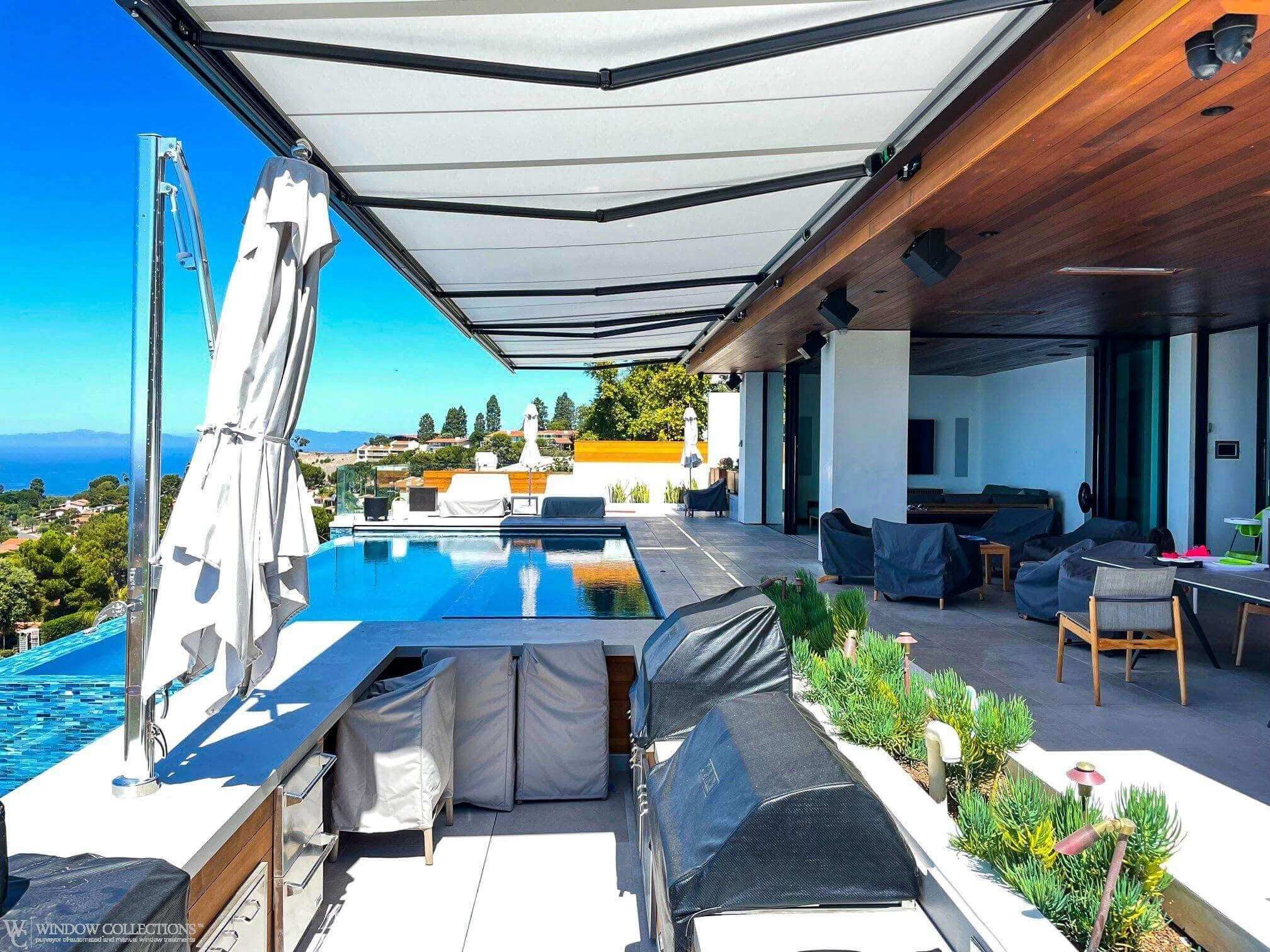 Modern patio with retractable awning, pool, and ocean view beside covered lounge area